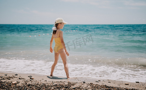 可爱的小女孩在清澈湛蓝的大海的映衬下沿着海边奔跑，在夏日的阳光下欢欣鼓舞。