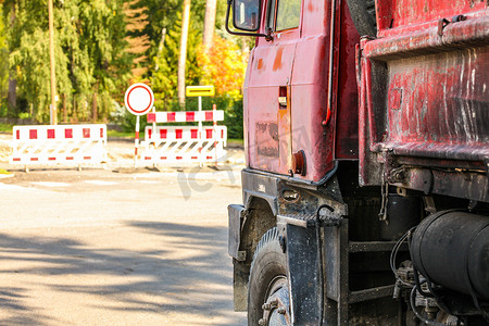 旧生锈和肮脏的红色卡车侧面的特写，货区墙上的油漆剥落，大轮胎可见，路障标志模糊，背景中的封闭路径。