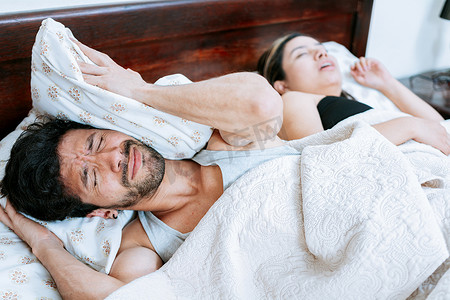 打呼噜摄影照片_女人在卧室里打鼾，丈夫捂着耳朵。