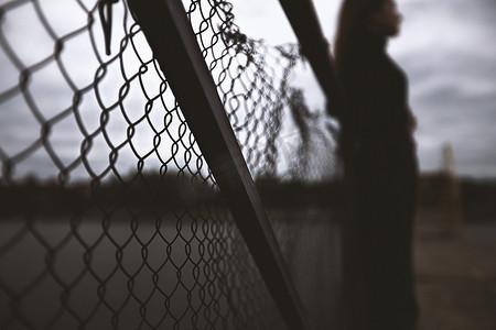 少女感摄影照片_年轻孤独的少女望着远方的铁网栅栏，独自放弃自己，在水边的码头上思考，感到无聊沮丧，晚上坐在码头上