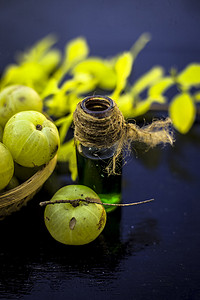 印度醋栗的特写镜头，其提取的精华或浓缩在木质表面的透明瓶中，水果和蔬菜篮中装有生醋栗。