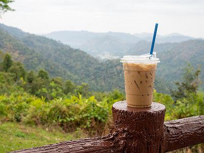 在群山和天空的映衬下，围栏上放着一杯冰咖啡。