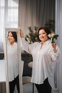 一位身穿白衬衫的成年女性站着，手里拿着洒有玫瑰的玻璃杯。