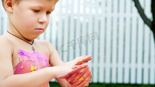 一个小孩，一个四岁的男孩在玩耍，用手指画画，装饰自己，在花园里，坐在毯子上，在草地上，草坪上，在夏天。