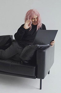 一个戴着粉色假发的男人坐在沙发上，通过笔记本电脑上的视频链接进行交流。