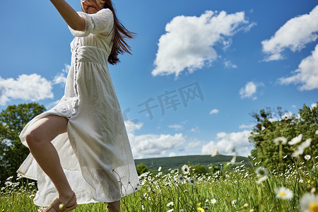 一个穿着浅色连衣裙的女人，在蓝天映衬下的洋甘菊花田中，从画面中跑开。