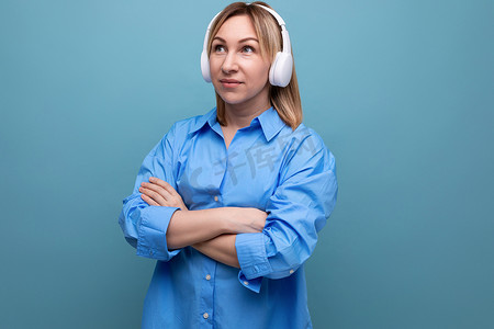 蓝色孤立背景中，穿着休闲衬衫的迷人欧洲女孩戴着白色大耳机听音乐