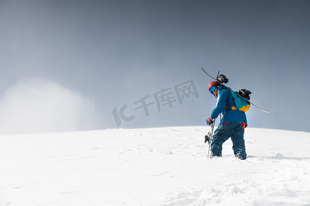男人滑雪摄影照片_滑雪设备和滑雪板的人爬上一座雪山。