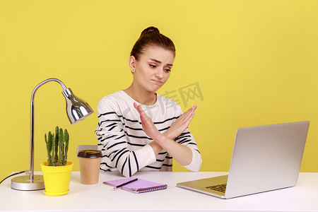 坐在工作场所的女性双手交叉显示 X 标志，皱着眉头看着笔记本电脑屏幕