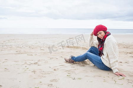 穿着时髦保暖衣服的微笑女人坐在沙滩上