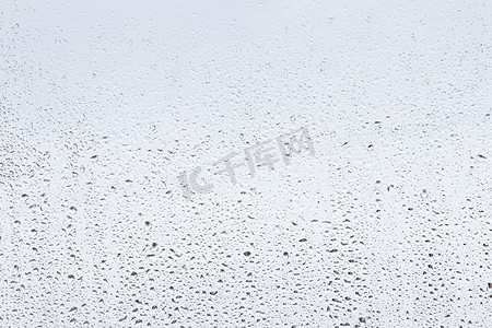 灰色天空背景下的雨滴落在窗户玻璃表面上。