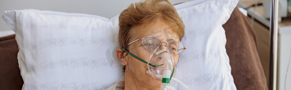 老年医生摄影照片_在 Covid-19 治疗期间，戴着呼吸面罩的老年女性患者躺在病房里