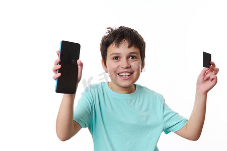 快乐的青春期男孩拿着智能手机和 ATM 卡，上面有促销文本的广告空间，在白色背景中突显
