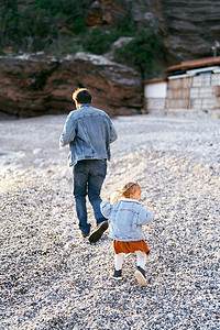 石子落下摄影照片_在落基山脉的背景下，小女孩在圆石滩上追着爸爸。