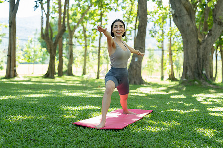 公园健身摄影照片_年轻迷人的女孩正在公园中央的健身垫上做高级瑜伽体式。