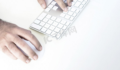 男性手点击鼠标并在白桌上的白色键盘上打字