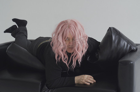 一个戴着粉红色假发的醉汉躺在沙发上，正在醒来。