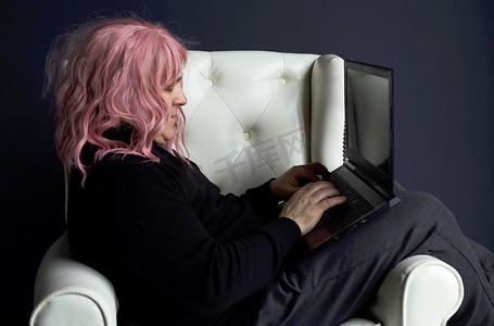 一个戴粉色假发的男人坐在白色椅子上，在电脑前工作