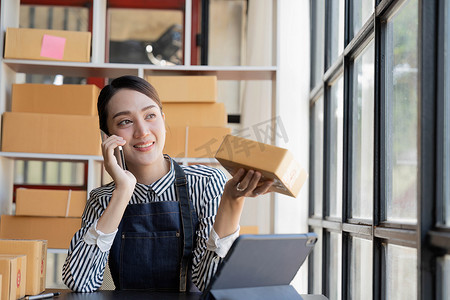 亚洲女性正在与客户通电话以确认订单，她拥有一家网上商店，她通过一家私营运输公司打包和运送。