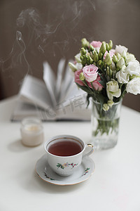 春天的静物画，花瓶里的一束玫瑰，白桌上的一杯茶和一本书。