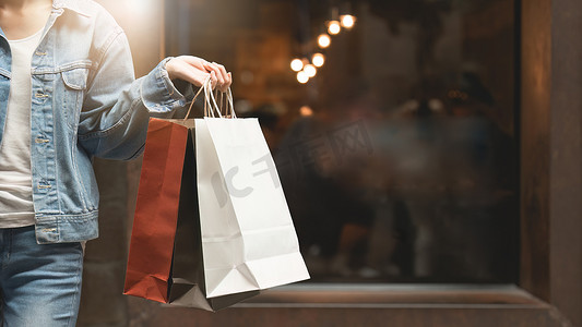 限时返场摄影照片_亚洲时尚女性提着购物袋在购物中心散步，同时进行限时促销