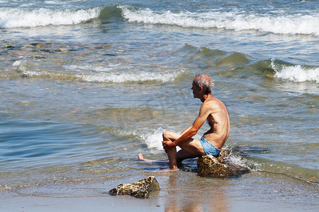 保加利亚瓦尔纳 — 2020年7月19日：年长瘦弱的男性瑜伽士坐在海中的岩石上