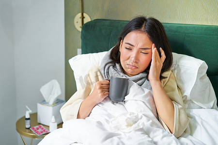 亚洲女性头痛、感冒、在家请病假、躺在床上、喝热茶、患流感的肖像