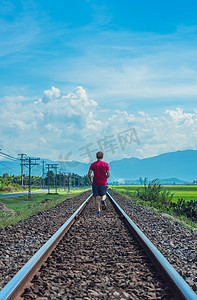 在阳光下奔跑摄影照片_男人在铁轨上奔跑，明媚的夏日阳光下风景红 T 恤短裤后视