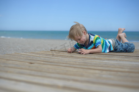 沙滩上的孩子摄影照片_男孩躺在沙滩上的木走道上