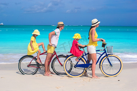 年轻的父母和孩子在热带白沙滩上骑自行车