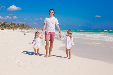 快乐的父亲和他可爱的小女儿在阳光明媚的日子里在白色沙滩上散步