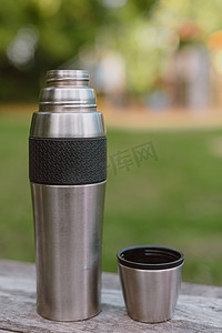 不锈钢杯，带热水瓶的杯子站在绿色自然背景下森林的木桌上。