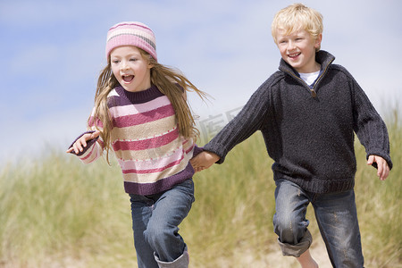 两个在沙滩上奔跑的小孩手牵着手微笑