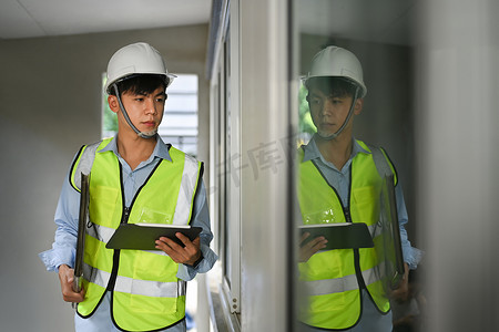 工程师戴安全帽和黄色背心拿着剪贴板检查建筑工地的画像
