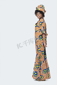 身着非洲印花服装的年轻女性站在灰色背景上的全长肖像