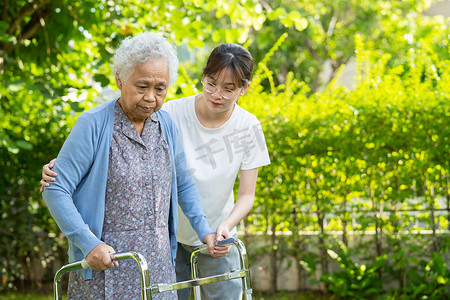 照顾者帮助和照顾亚洲老年人或老年老妇人在愉快的新鲜假期中在公园散步时使用身体强壮的助行器。
