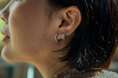 银耳环摄影照片_戴漂亮银耳环的年轻女子的细节。
