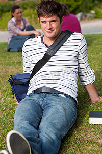 英俊的男学生背着书包躺在草地上