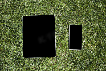 草地上的空白平板电脑和手机