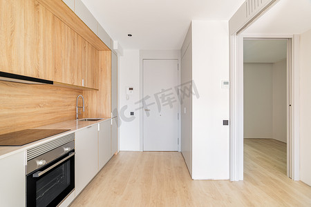一室公寓沿墙的简单小型模块化厨房区，靠近前门和通往空卧室的门口。