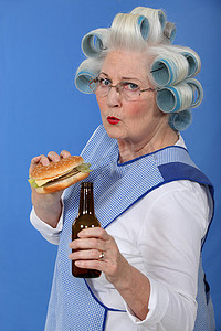 汉堡卷摄影照片_带卷发器的奶奶一边品尝芝士汉堡一边喝啤酒的搞笑图片