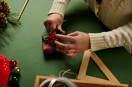 特写女性用红色礼品纸包裹圣诞小礼物，用绿色装饰胶带绑起来，系上蝴蝶结