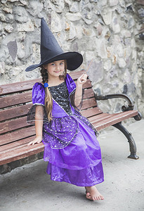 魔杖摄影照片_迷人的年轻女巫拿着一根魔杖坐在长凳上