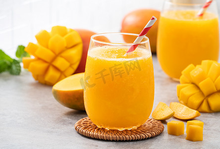 红色果汁摄影照片_灰色桌子背景上的玻璃杯中的新鲜芒果汁冰沙。