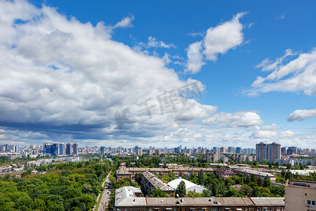 一个城市景观，在城市的一个老住宅区有一个绿色公园，在明亮的蓝天和厚厚的云层的映衬下，地平线上有新建筑。