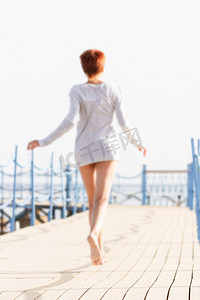 红色短发的年轻女子在木码头上奔跑。