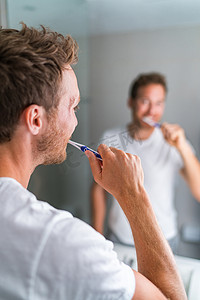 早上刷牙的人用牙刷和牙膏看着浴室镜子。