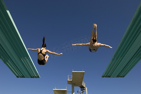 两名女性在湛蓝的天空下从跳水板上跳水的后视图