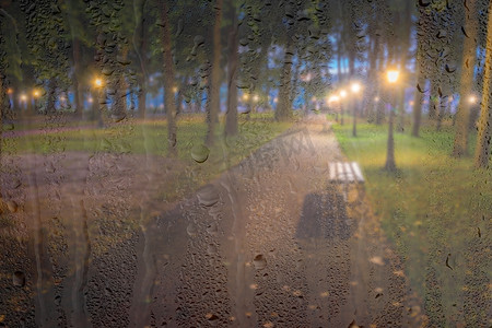 在雨天、湿漉漉的后面，灯笼和长椅散焦的夜间公园