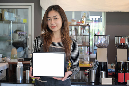 穿着围裙的年轻女企业家站在现代咖啡馆里展示数字平板电脑。